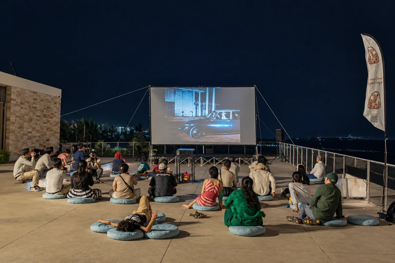 Audience on floor cushions watching an outdoor film screening on a rooftop at night
