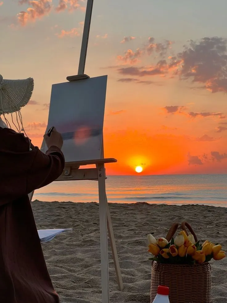 An artist painting a sunset on the beach at an easel