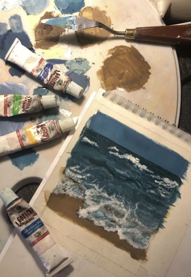 A seascape painting in progress among paint tubes