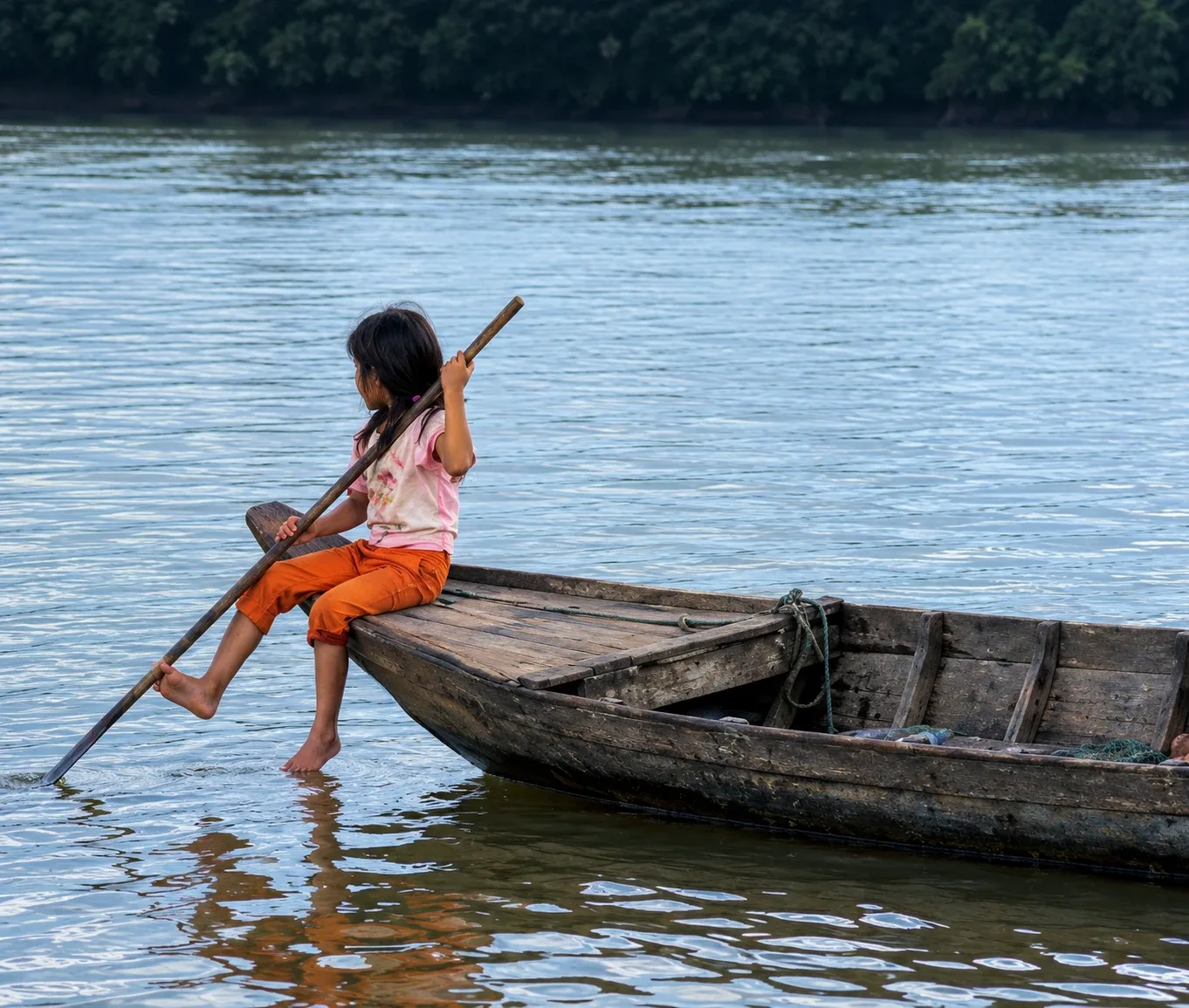 A child paddling a wooden boat on calm water